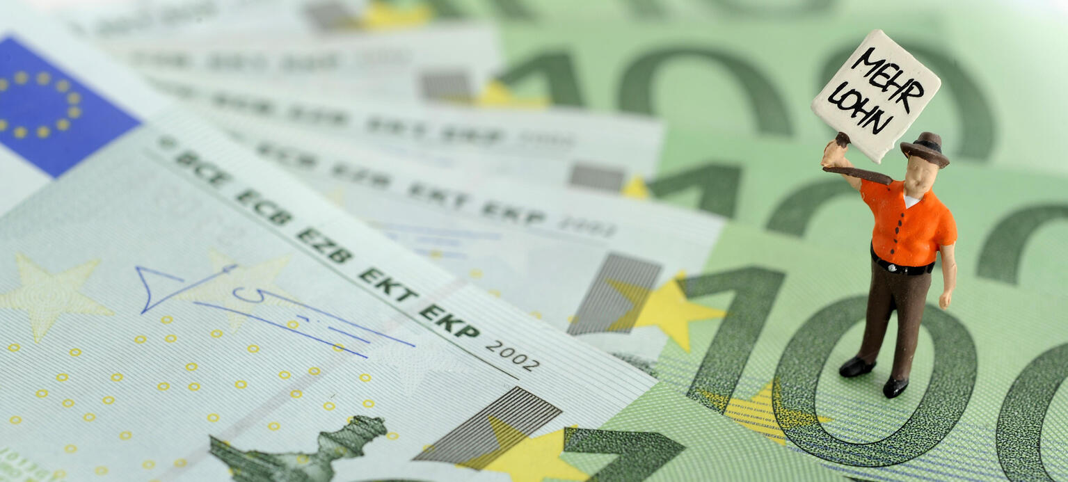 Figur auf 100 Euro-Scheinen hält Transparent 'Mehr Lohn'