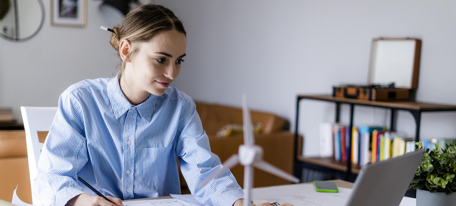 Woman in office working on plan and laptop with wind turbine model on table