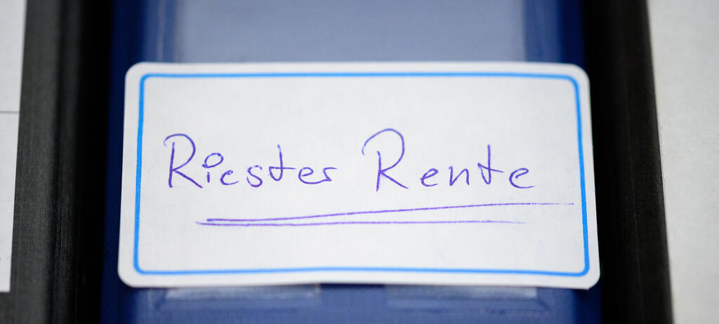 Ein Ordner mit einem Aufkleber 'Riester-Rente' steht in einem Regal.