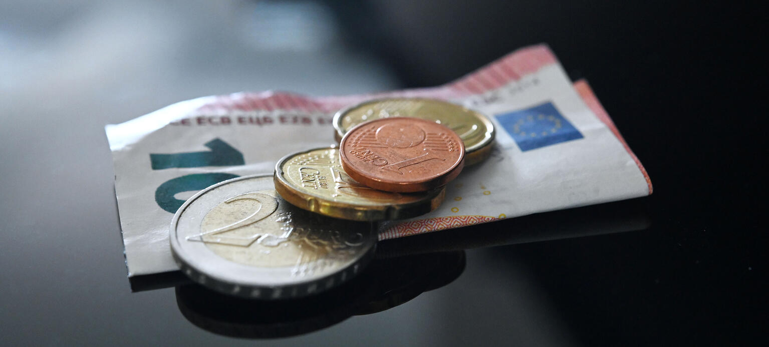 Münzen und ein Geldschein im Wert von 12,41 Euro liegen auf einer schwarzen Fläche. Dies entspricht dem Mindestlohn seit dem 01.01.2024 in Deutschland - Mindestlohnreport