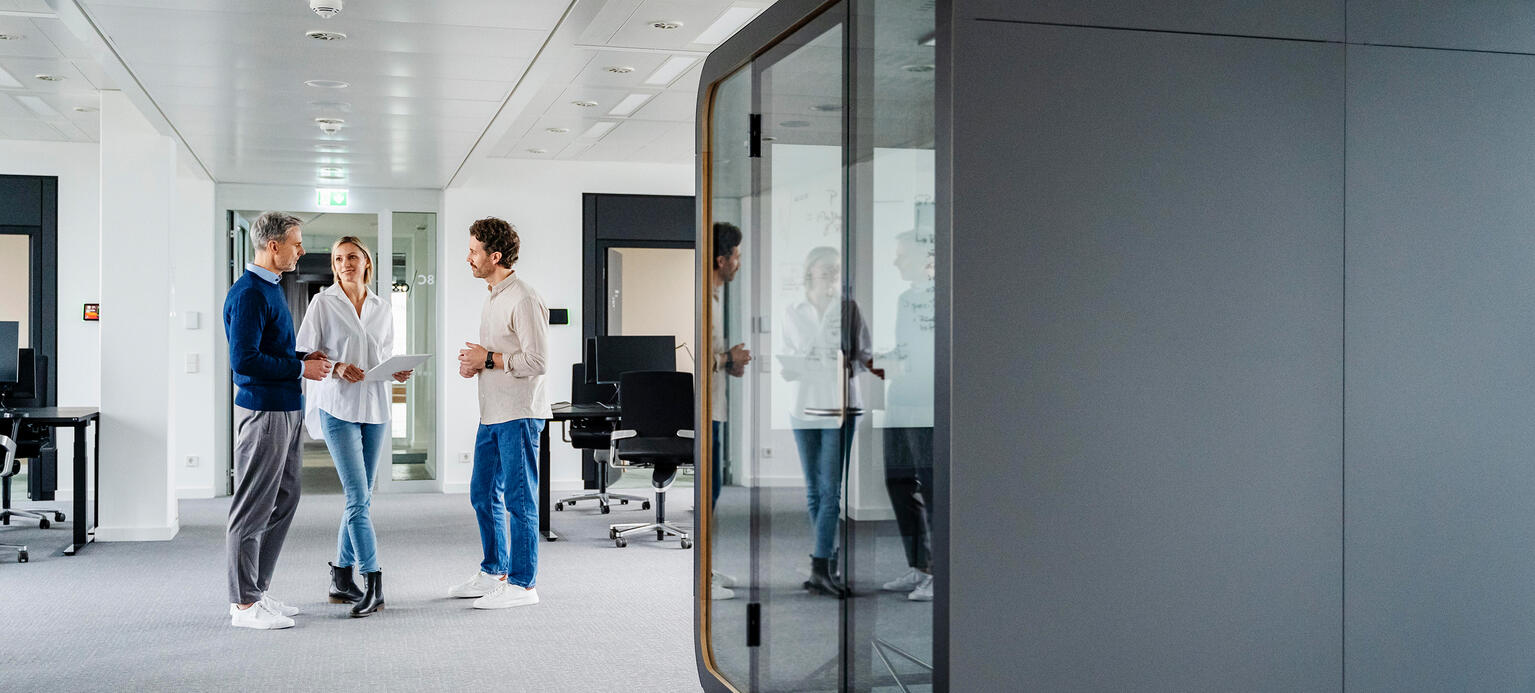 Drei Kollegen stehen in einem Büro zusammen im Raum.