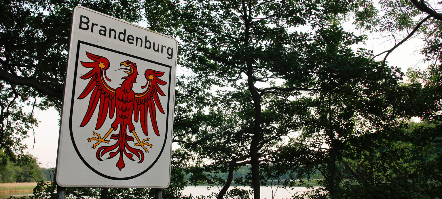 Schild Bundesland Brandenburg mit typischer Seenlandschaft im Hintergrund