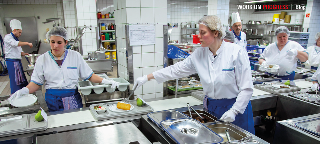 Grossküche im Krankenhaus. Das Mittagessen wird am Fliessband auf Tabletts verteilt.